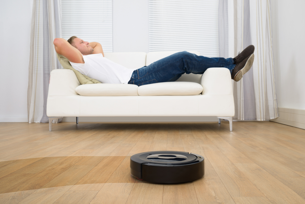 a man relaxing in his home while the robot vacuum is cleaning the floor