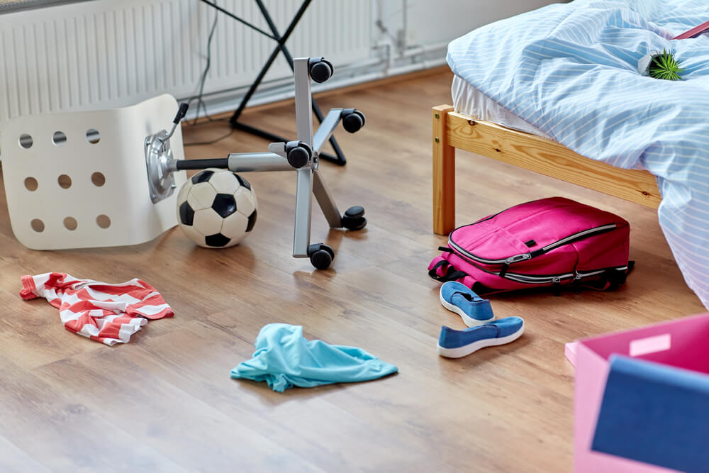 kids room with scattered toys, clothes, and bag where robot vacuum gets stuck