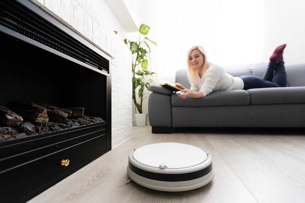a woman operating her robotic vacuum cleaner while laying on the sofa